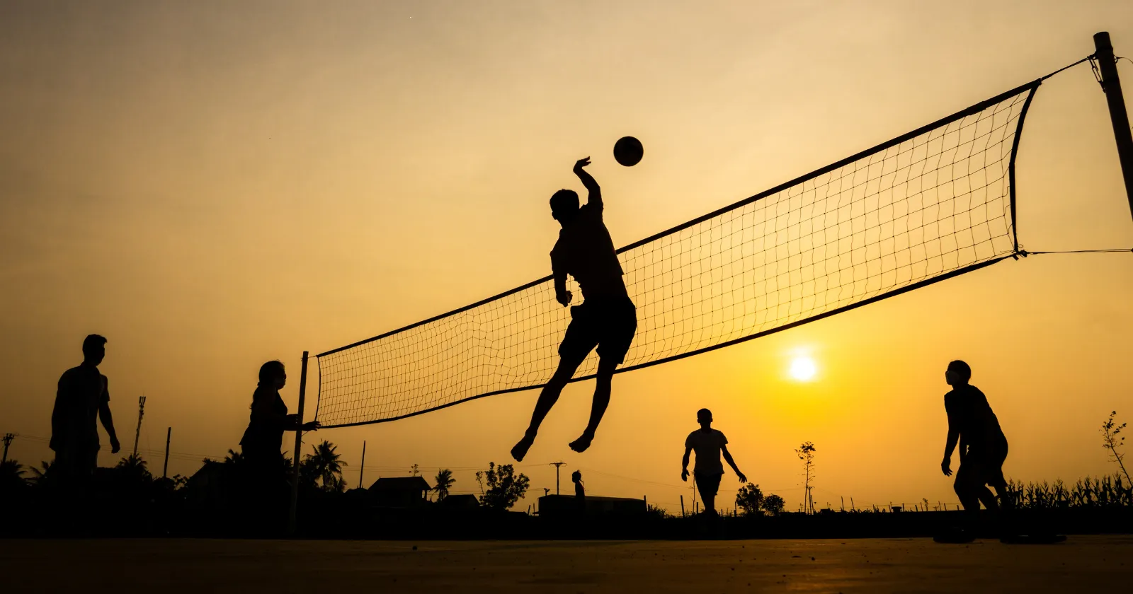 Joueurs de beach-volley sautant au coucher du soleil