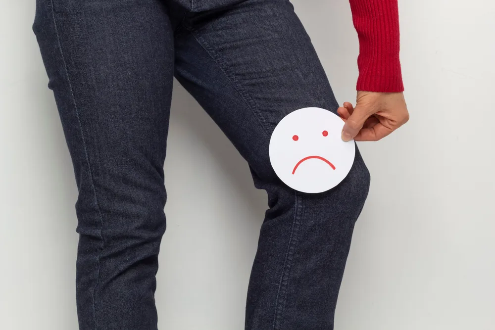 Personne au genou douloureux tenant un visage triste en papier